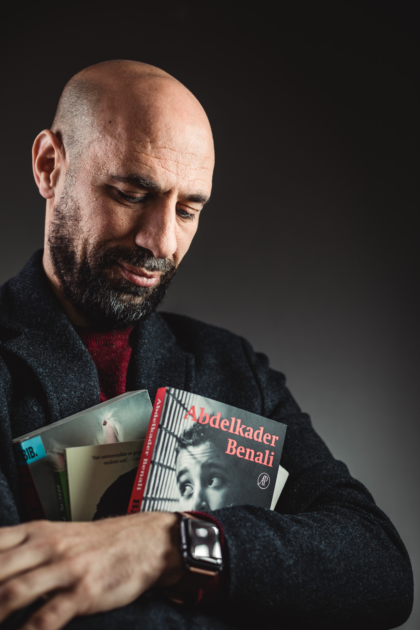 Portret van auteur Abdelkader Benali. Hij kijkt naar enkele van zijn geschreven boeken die hij in zijn armen houdt.
